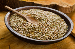 A bowl of dried lentils with wooden spoon.