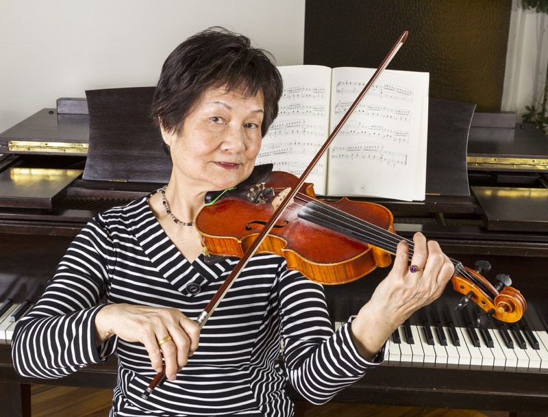 Woman sitting in front of piano playing the violin